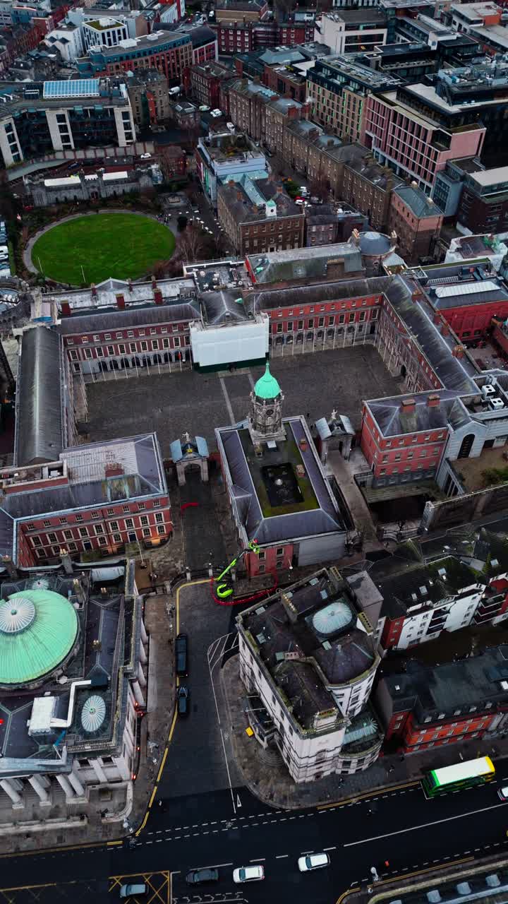 Drone shot over Dublin castle in the city centre in Ireland with busy streets below with cars and buses and tourists walking around in Irish cityscape on cloudy overcast day in winter