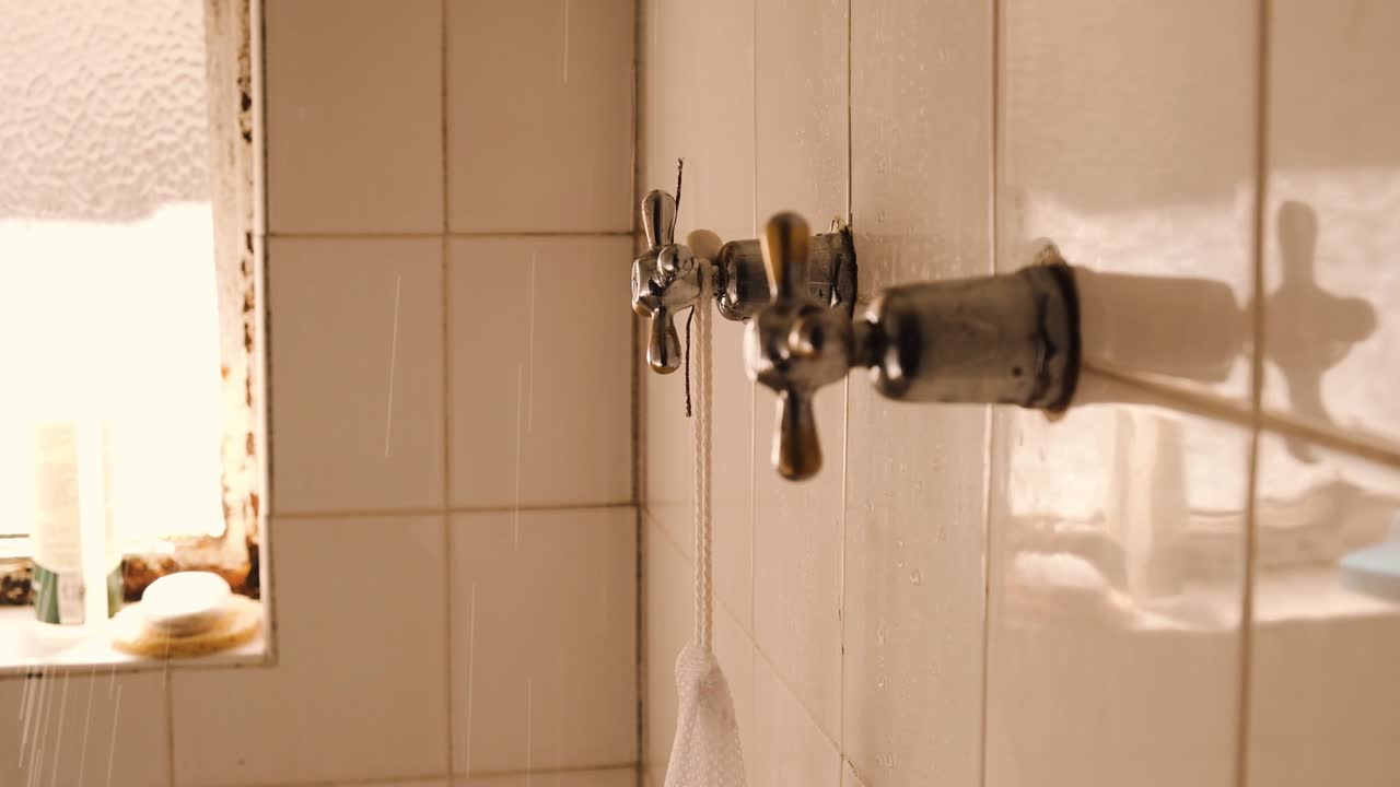 girando a mano el grifo del baño haciendo rociar el agua de la ducha en la pared de azulejos blancos