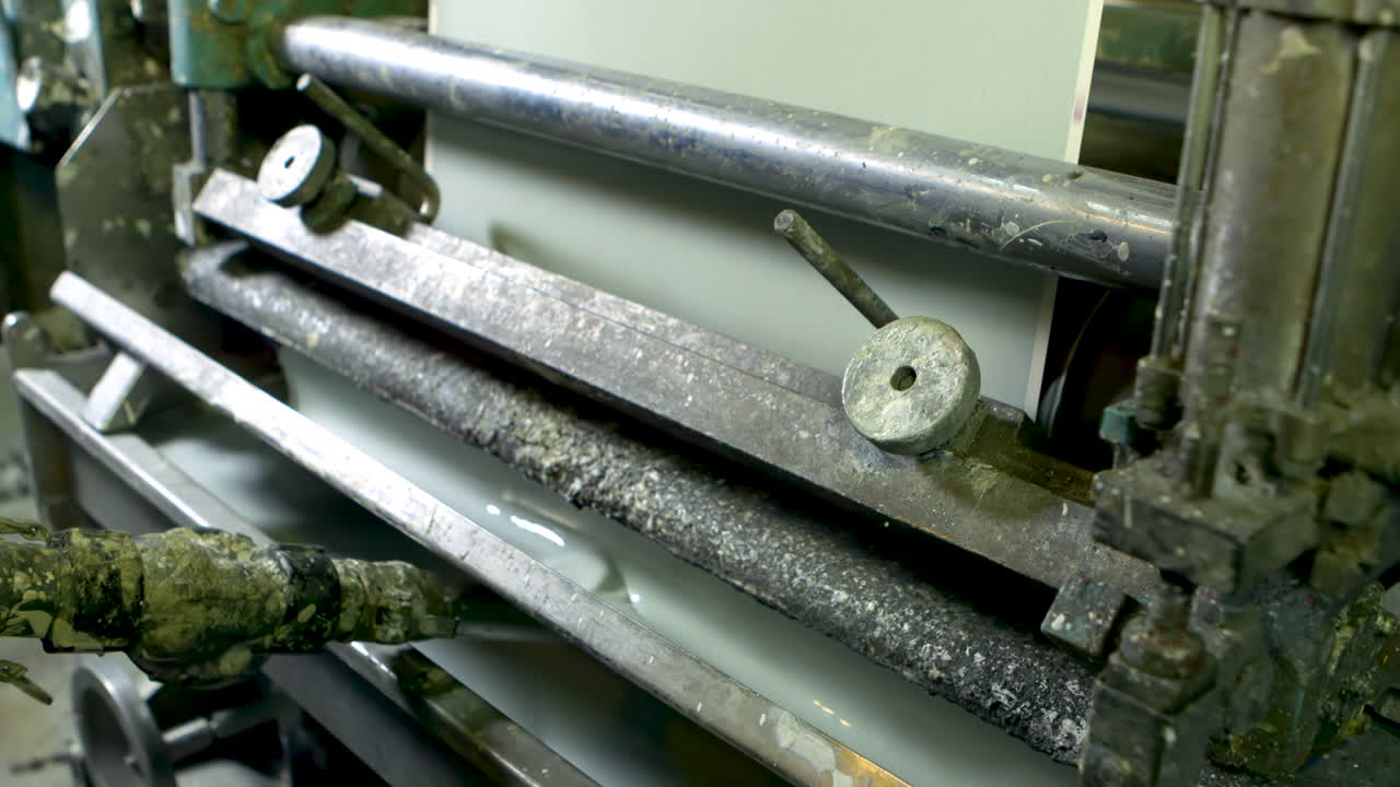 Medium shot of an old and well-worn machine printing green wallpaper, using a tray of liquid light green paint.