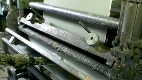 medium shot of an old and well-worn machine printing green wallpaper, using a tray of liquid light green paint.