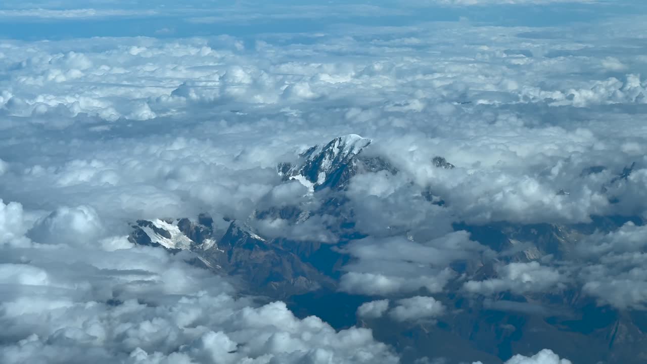 An elevated aerial view taken from a jet cockpit flying near the summit of the Mont Blanc, with few snow, in a summer morning, surroended by cottony clouds