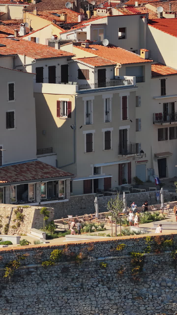Aerial drone view of Antibes Old Town houses with terracotta rooftops and seaside promenade, with visitors enjoying the historic coastal atmosphere. Vertical