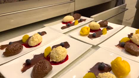 mano del chef que sirve un delicioso postre con mousse de chocolate y vainilla, sorbete de mango y salsa de frambuesa