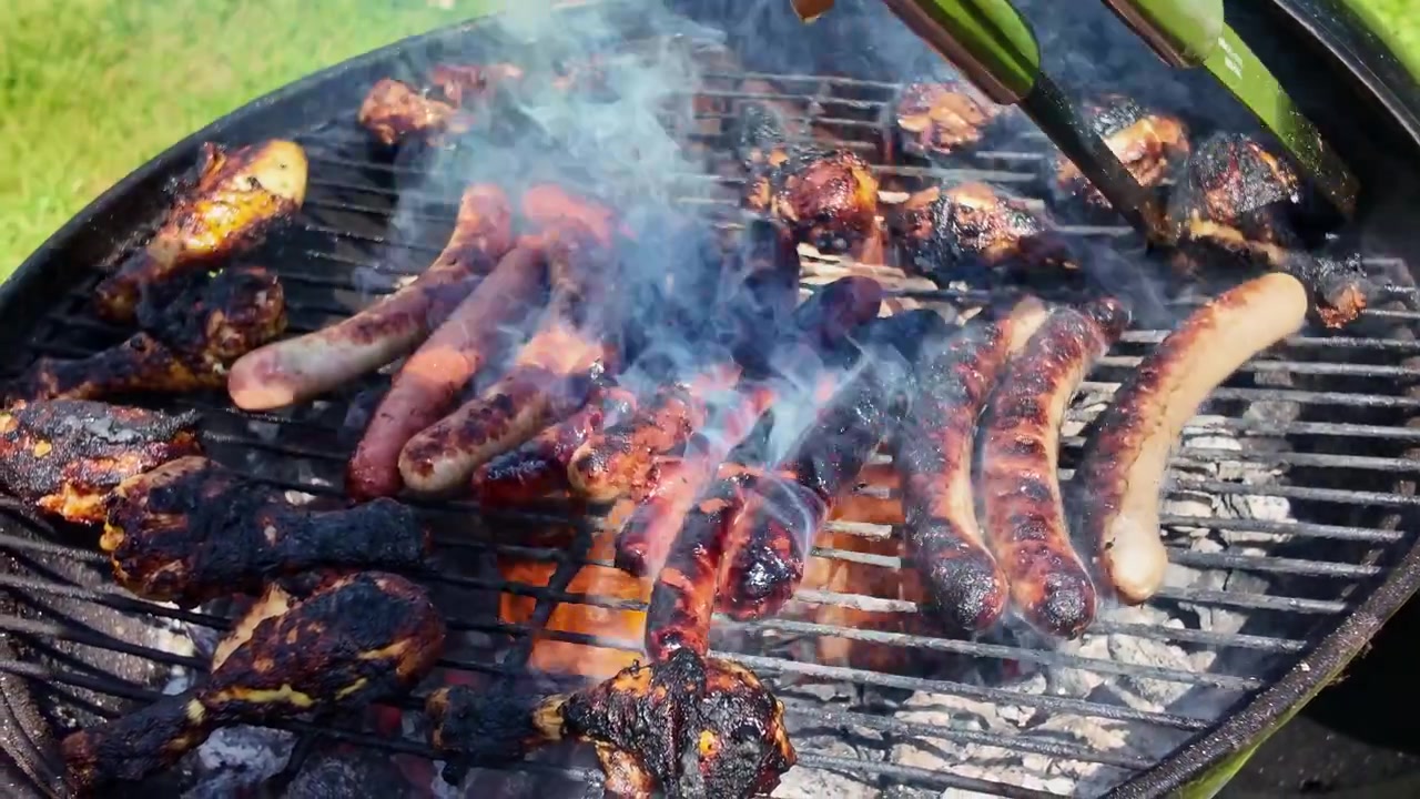 Salsicce e carni alla griglia che cuociono su un barbecue fumante durante un raduno primaverile in un giardino all'aperto