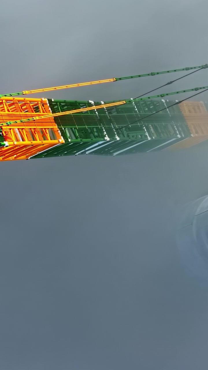 Braccio colorato di una gru che scompare nella fitta nebbia e nel cielo nebbioso, panoramica verticale dall'alto con drone.
