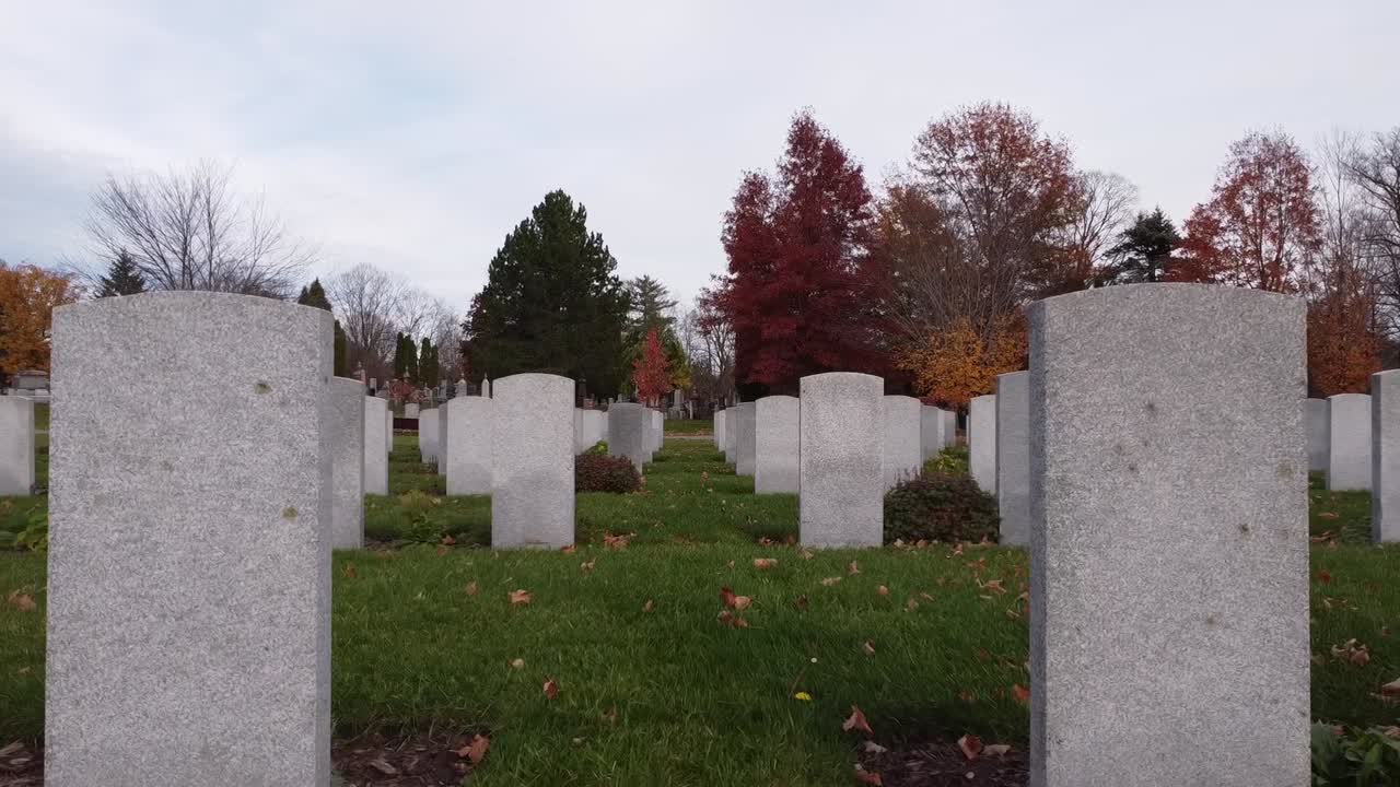 Drone flies through headstones at a cemetery during autumn.