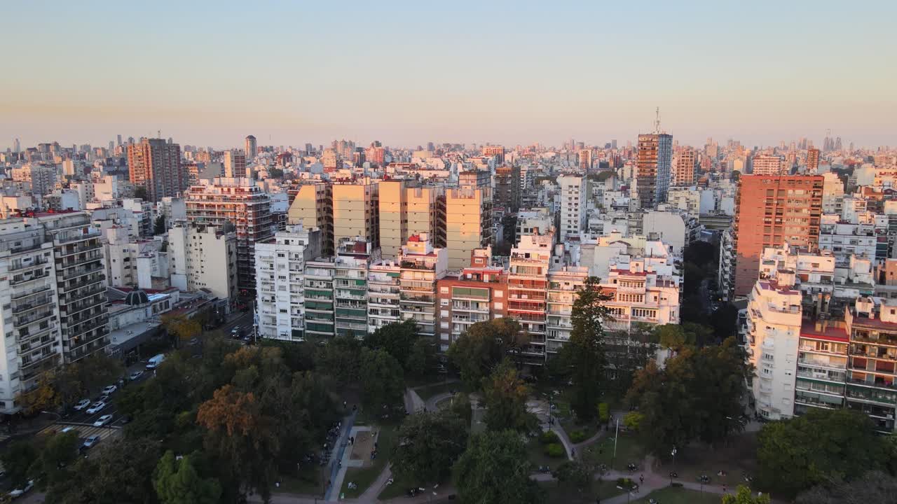 Residential blocks in residential area and visible paths and trees from Parque Rivadavia, Buenos Aires. Aerial dolly in bird's-eye view during golden hour.