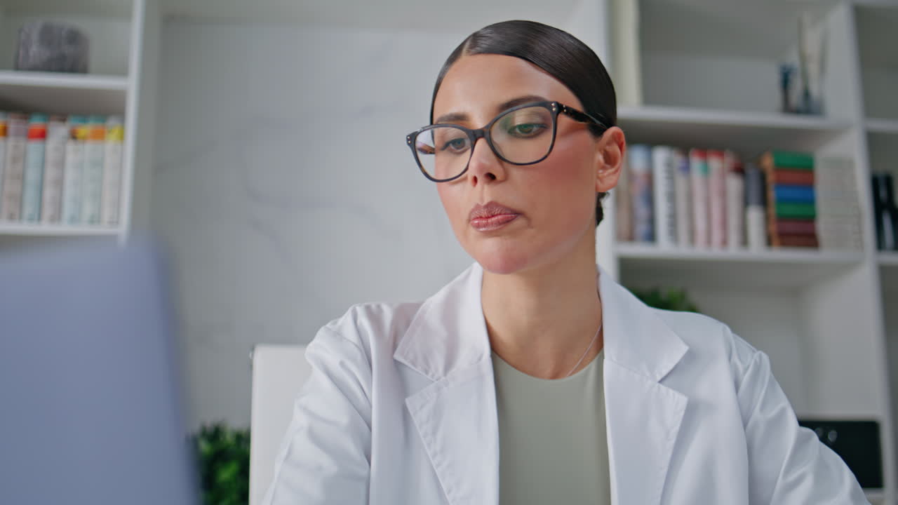 Serious therapist talking videocall by laptop in clinic closeup. Woman doctor