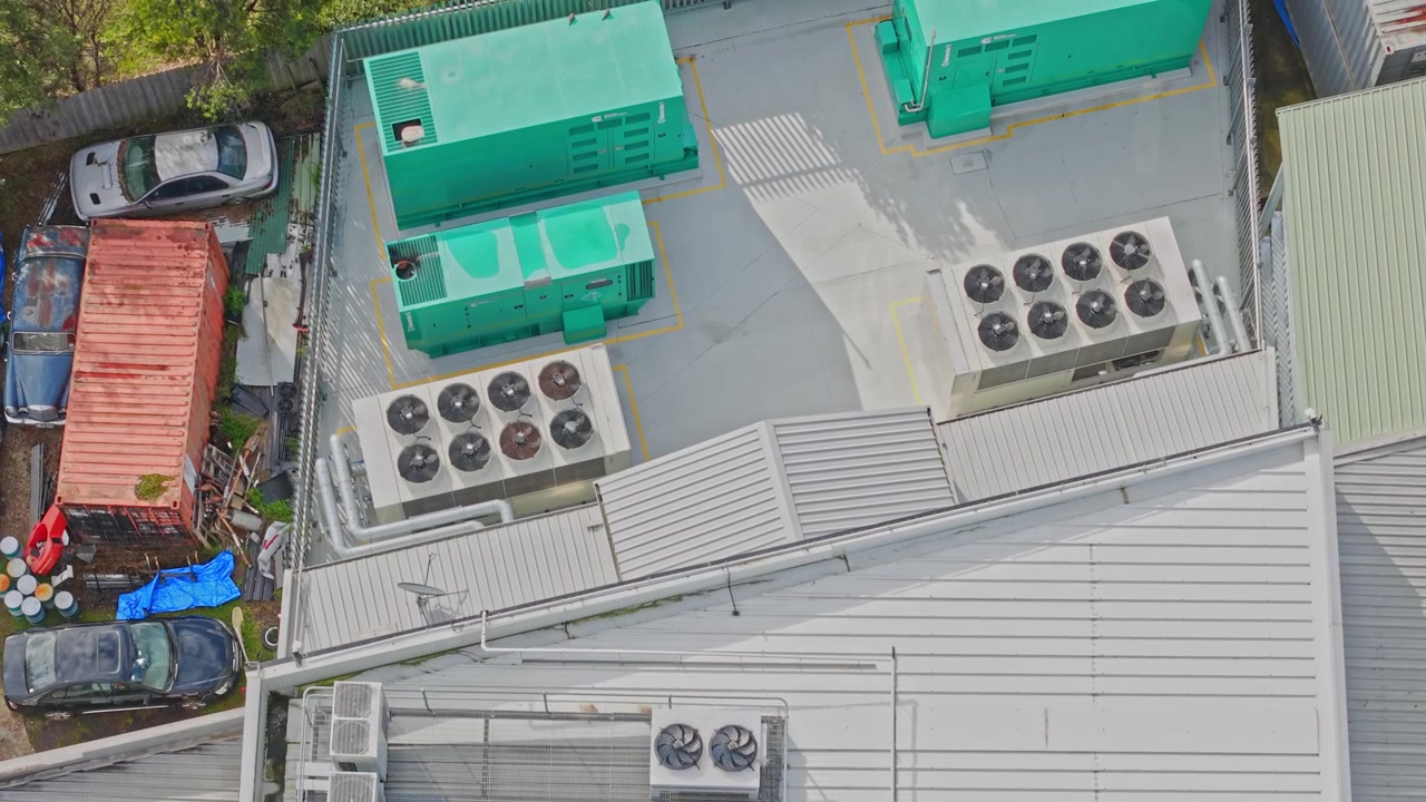 Drone video reveals a modern data center rooftop with industrial HVAC units, green backup generators, and metal roofing, shot in bright daylight for a crisp, clean technical look.