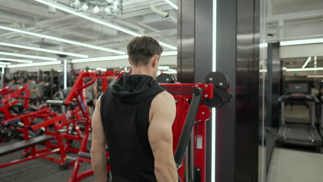 mascular adult male perform shoulder side raise exercise in machine at fitness center - rear view