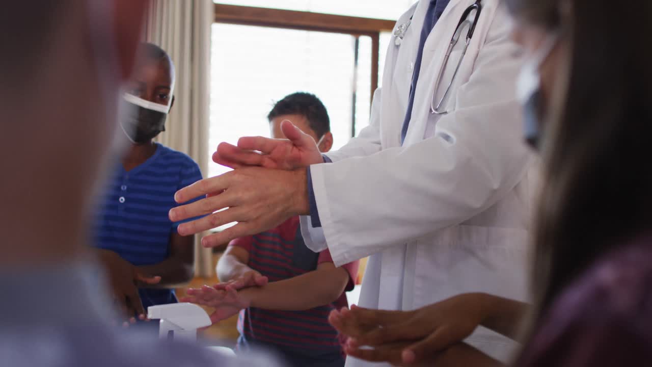 다양한 학교 선생님과 학교 아이들이 서서 손을 소독하고, 모두 얼굴 마스크를 착용하고 있습니다.