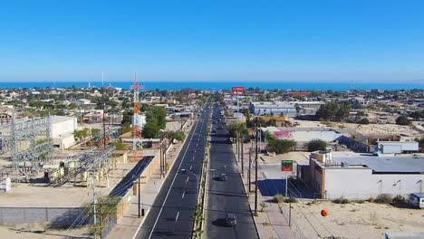 Vista-De-Un-Dron-Inclinado-Sobre-Una-Carretera-Que-Muestra-Un-Pueblo-Cerca-De-La-Costa