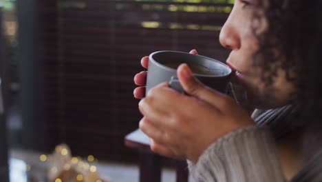 close up of african american woman drinking coffee while sitting near the fireplace at vacation home