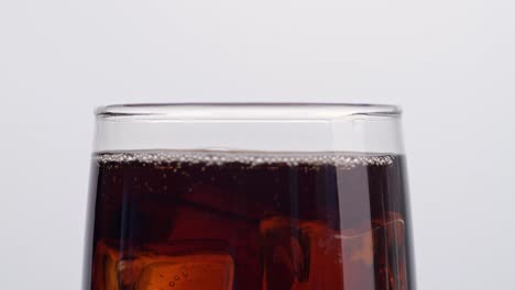 close up of ice cubes falling in a glass of fresh cola on white background