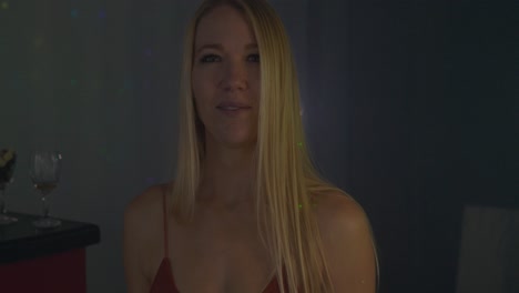 hermosa rubia caucásica mujer blanca frente a una pared de luz led en una oscura escena de club nocturno mirando y caminando directamente hacia y hacia la cámara con una mirada coqueta y coqueta.