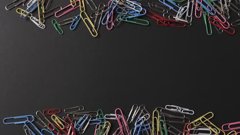 overhead view of scattered colourful paper clips with copy space on black background, in slow motion