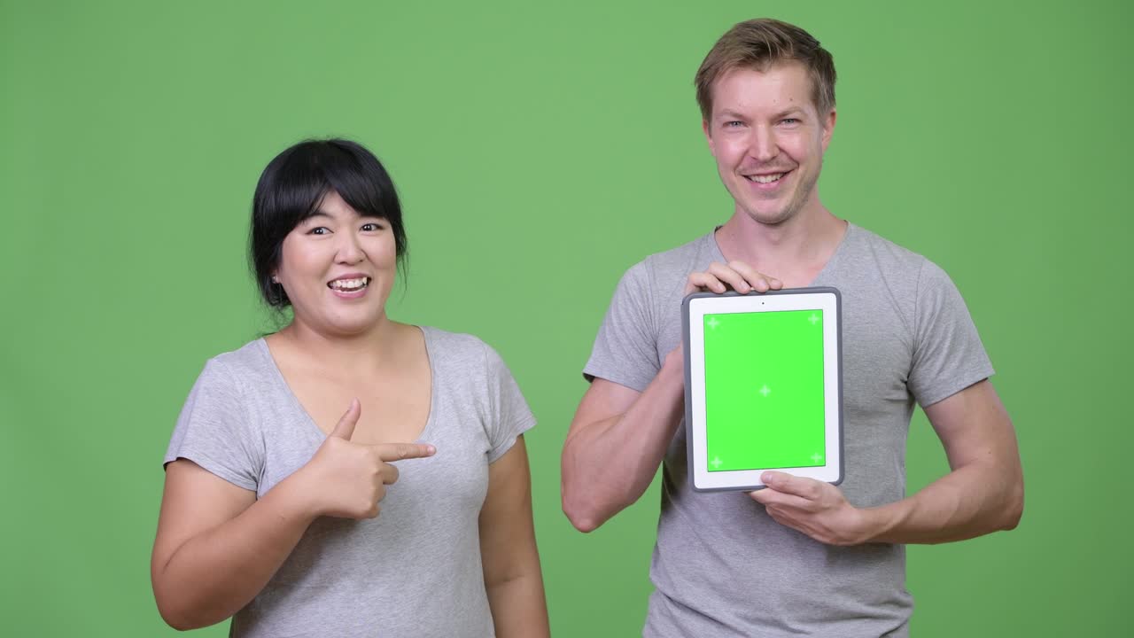 Young happy multi-ethnic couple showing digital tablet and giving thumbs up together