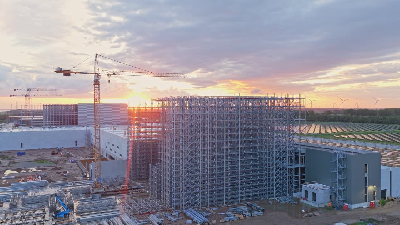 Crane atop active site at sunrise, warehouse structure climbs steadily