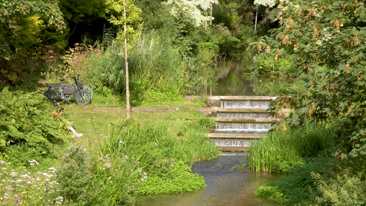A bicycle rests near a canal and footbridge surrounded by lush greenery and trees