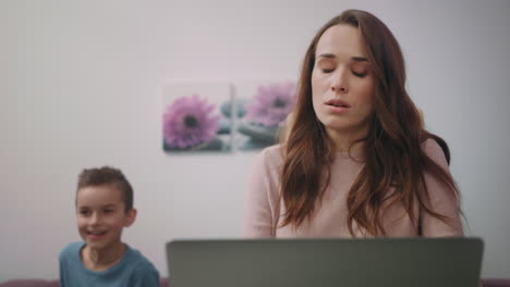 tired mother working on laptop at home. boy interrupt busy mom