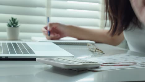 young woman calculating monthly home expenses, tax, credit card bills payment and bank account balance in living room at home.managing budget, entering data in computer application.