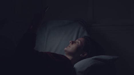 woman using phone in bed at night