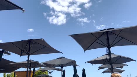 Sombrillas-De-Playa-Balanceándose-Frenéticamente-En-El-Fuerte-Viento-En-Un-Día-Muy-Soleado-Con-El-Cielo-Azul-De-Fondo