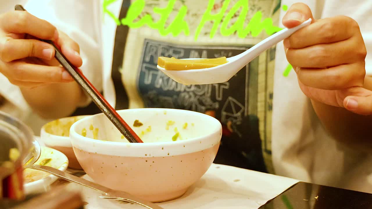 Person savoring hotpot soup with chopsticks
