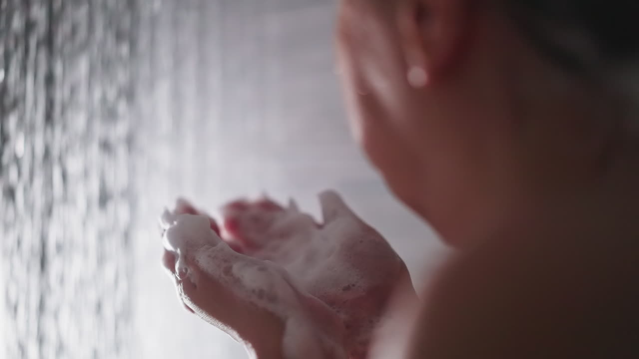 여성이 샤워 물 에서 손에서 거품을 불어 넣습니다. 여성은 부드러운 비누 거품으로 게임을 즐기고 집 화장실에서 목욕을합니다. 화장실 의식