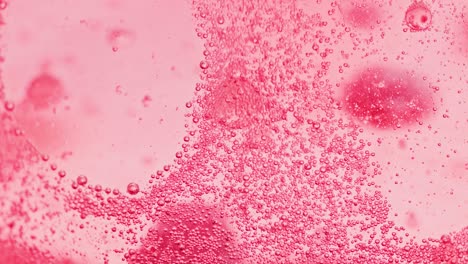 macro shot of many small red bubbles sparkling in water and a big bubble falling to ground out of focus with a bright background