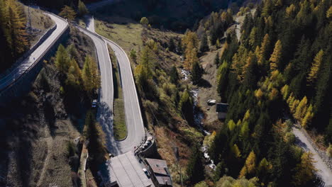 A-valley-with-green-fresh-forest-and-river-streaming-and-a-zigzag-road-with-a-village,-top-aerial-view