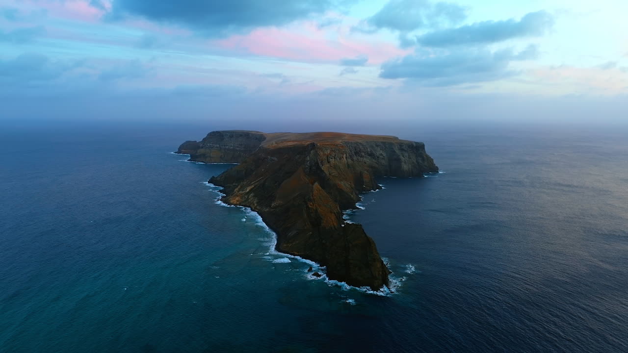 Bare rock island in the waters of the North Atlantic Ocean. White waves crash by the steep mountains. The Madeira Islands, Portugal. Aerial view.
