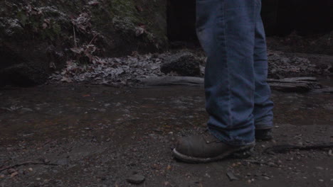 close up of a hikers boots as he approaches a stream where he reaches into his backpack to retrieve a tin cup to get water from the creek