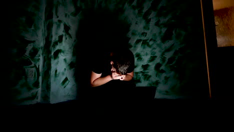 depressed teenager in dark corner of room reading hate messages on laptop and cover his face, cyberbullying concept