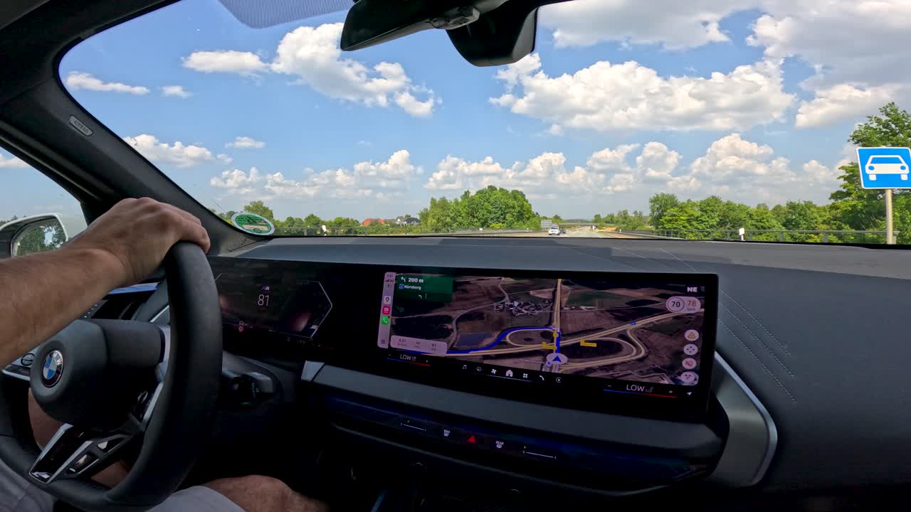 Driver steers through roundabout using dashboard navigation, sunny day, wide interior view, smooth motion