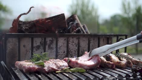 tong turning ribs with rosemary on the fire bbq grill