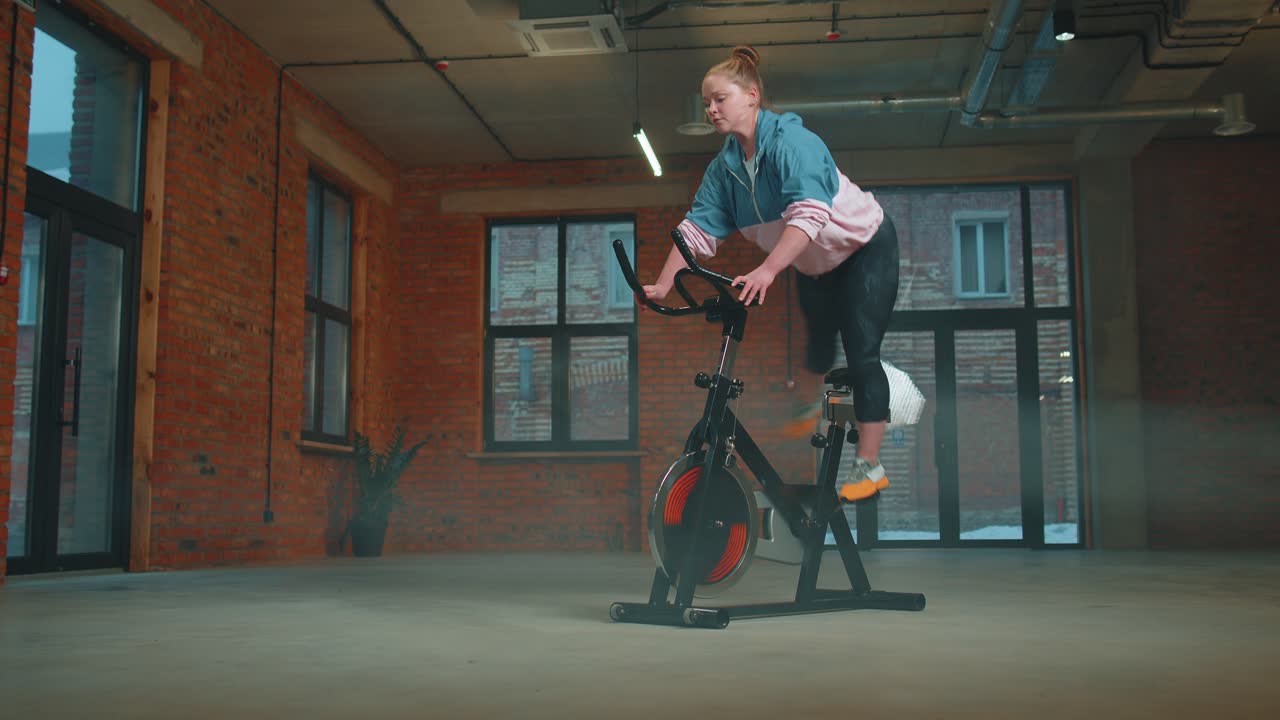 Healthy caucasian woman exercising workout on stationary cycling machine bike in gym slow motion