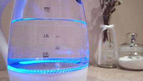 Water-boiling-with-bubbles-in-the-bottom-of-neon-electric-kettle,-close-up