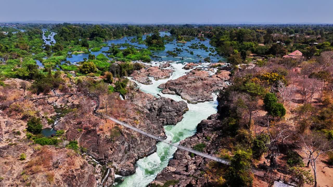 Drone pulls away over turbulent Mekong rapids near Don Det, Laos, revealing fractured basalt flows, rocky fault lines, and scattered islets across the braided floodplain in uplifted Champasak Plateau
