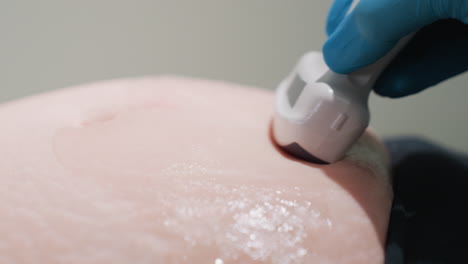 close up of lab scientist wearing blue gloves using ultrasound transducer to professionally examine abdomen of patient during diagnostic procedure showing scanning gel for clear imaging