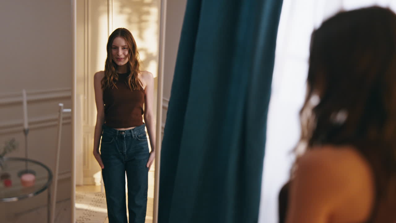 미소 짓는 소녀가 큰 청바지를 입고 거울을 바라보고 행복한 젊은 여성이 존경하는 점프