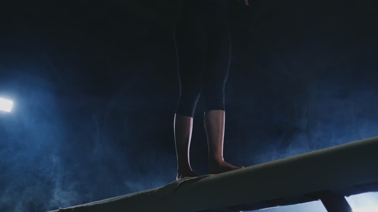 Girl gymnast practicing on a balance beam in gym.
