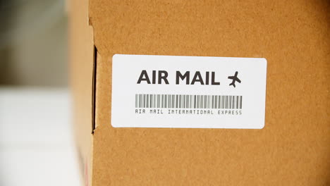 manos aplicando etiqueta adhesiva de correo aéreo en un buzón de cartón con código de barras expreso internacional