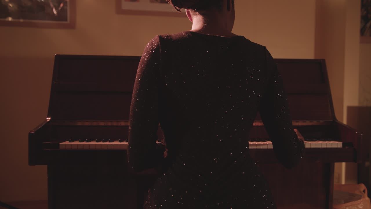 Female Pianist In Glittery Dress Sits In Front Of A Piano And Plays - back view, medium shot