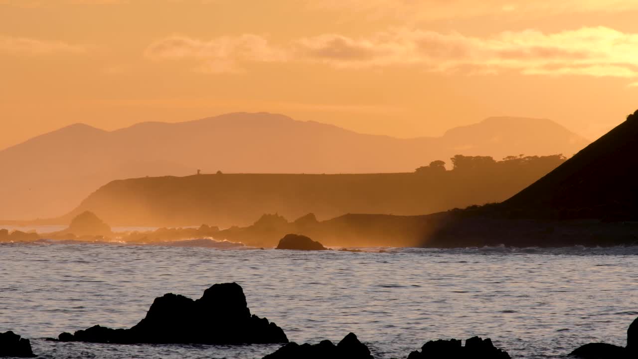 impresionante puesta de sol dorada sobre el mar al anochecer con olas, aerosol del océano y capas de montañas en wellington, nueva zelanda aotearoa