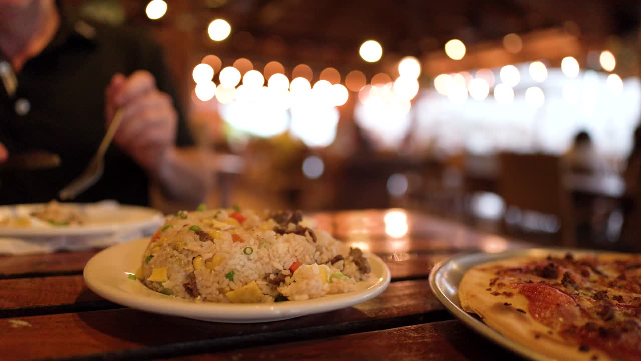 Close-up shot of a person eating fried rice at an outdoor restaurant with bokeh lighting
