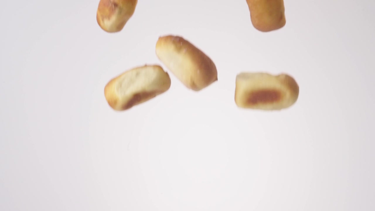 Kolaches salati dorati che cadono a cascata e attraversano l'inquadratura su sfondo bianco al rallentatore. Annunci di catering per la colazione, post per menu brunch, spot pubblicitari per snack salati.