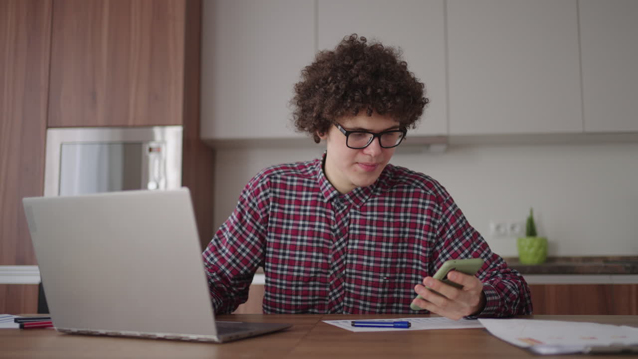 Young man with smartphone in his hands. Modern businessman or student at home office. Freelancer at work. Young student man study at home with laptop and uses a smartphone