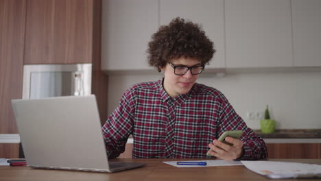 joven con un teléfono inteligente en sus manos. hombre de negocios moderno o estudiante en la oficina de casa. profesional independiente en el trabajo. joven estudiante estudia en casa con una computadora portátil y usa un teléfono inteligente