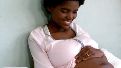 pregnant woman sitting on bed touching her belly